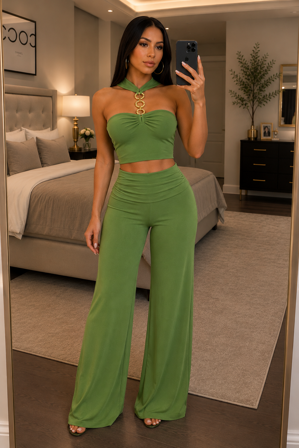 A woman takes a mirror selfie in a bedroom wearing a matching olive green two-piece set consisting of a halter crop top and high-waisted wide-leg pants, accessorized with a gold circular necklace.