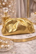 Gold clutch bag on a marble surface with jewelry and a mirror in the background