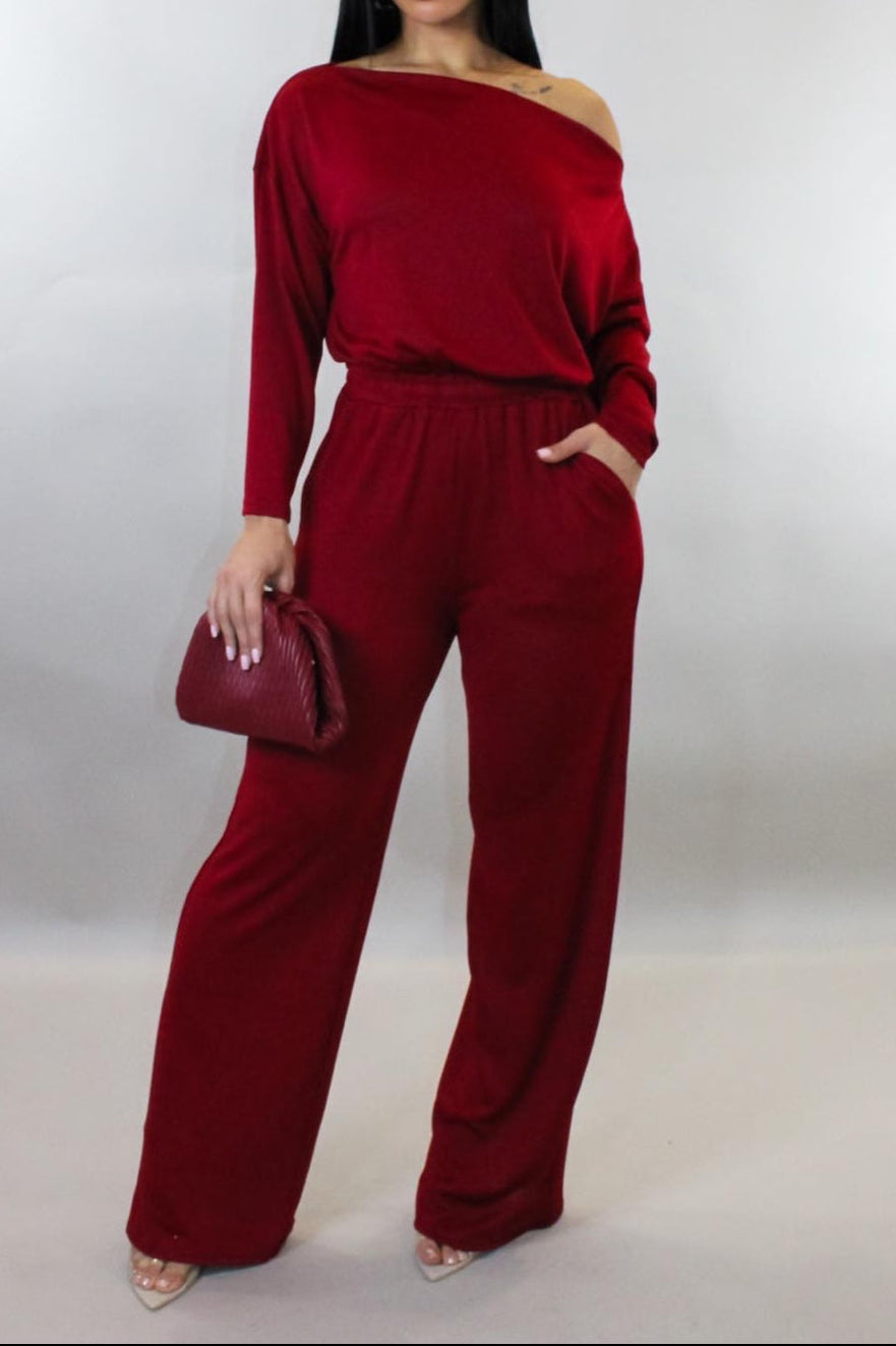 Woman wearing a red jumpsuit holding a matching handbag against a white background