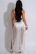 A woman shown from the back wearing a white sleeveless maxi dress with a long fringe skirt and cutout details, standing against a plain light background.