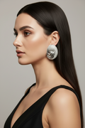 A woman in profile wearing a large, textured silver earring, shown against a neutral gray background.