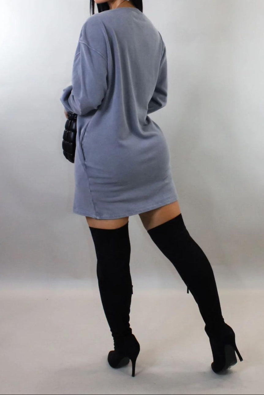 Woman wearing a gray dress with black knee-high boots on a plain background