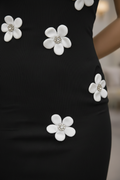 Close-up of a black ribbed dress with large white flower appliqués featuring crystal-like centers, worn by a model.