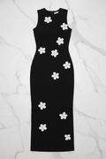 A sleeveless black midi dress with white flower appliqués, laid flat on a white marble background.