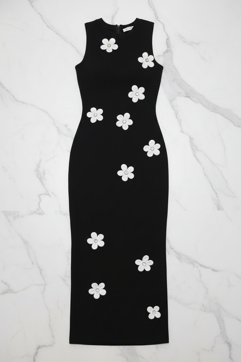 A sleeveless black midi dress with white flower appliqués, laid flat on a white marble background.