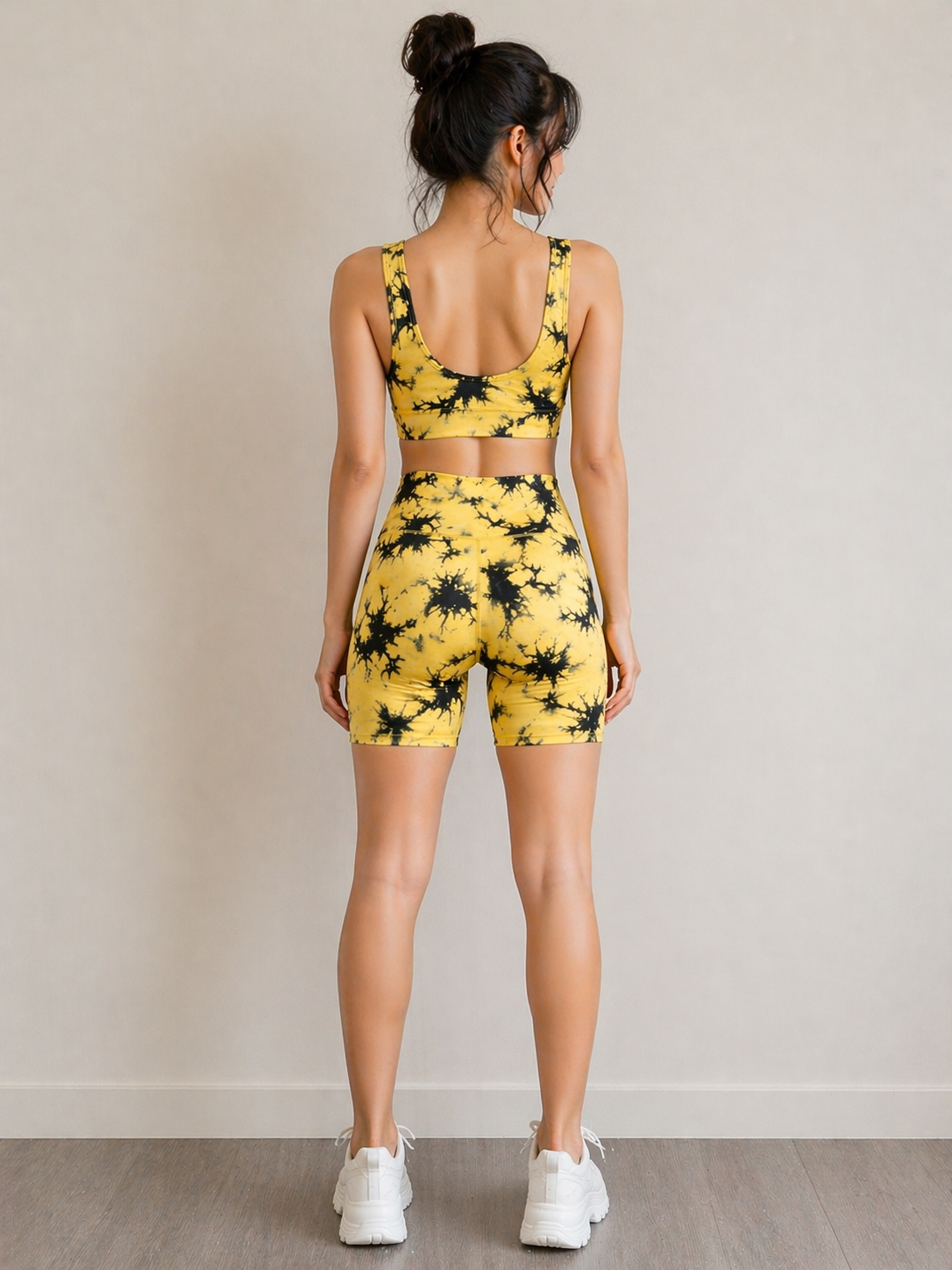 Woman wearing a yellow and black tie-dye sports bra and shorts set on a plain background