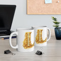 Two white mugs with gold letter 'L' design on a desk with office supplies.