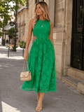 A woman walking on a city sidewalk wearing a sleeveless bright green lace midi dress with a fitted bodice and flared skirt. She is carrying a small woven beige handbag and wearing beige strappy heels.
