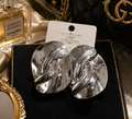 Silver earrings on a card with a Chanel perfume bottle in the background