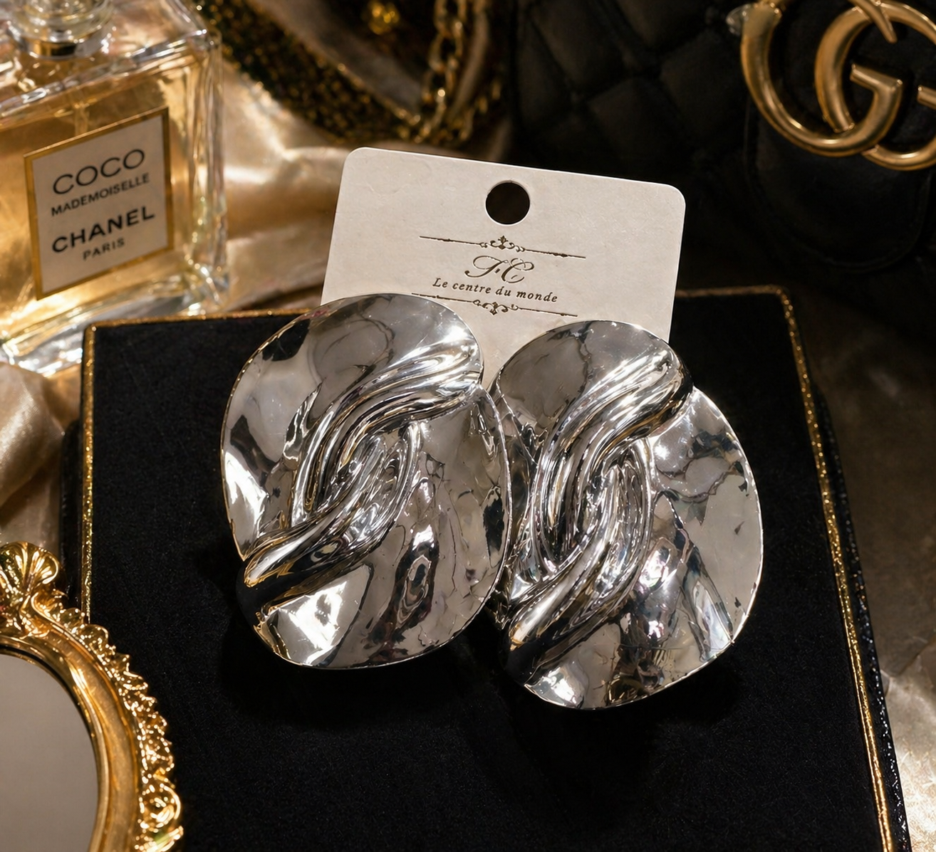 Silver earrings on a card with a Chanel perfume bottle in the background