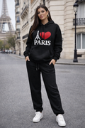 Woman wearing a black hoodie with 'I ❤️ PARIS' text and black pants on a street with Eiffel Tower in the background.