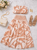 A two-piece women's outfit set featuring a peach and white abstract print crop top and matching high-waisted skirt, styled in a flat lay with a cream quilted handbag, gold earrings, beige sandals, and white roses on a light marble background.