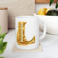 White mug with a gold letter 'L' design on a light surface with plants and a bowl in the background.