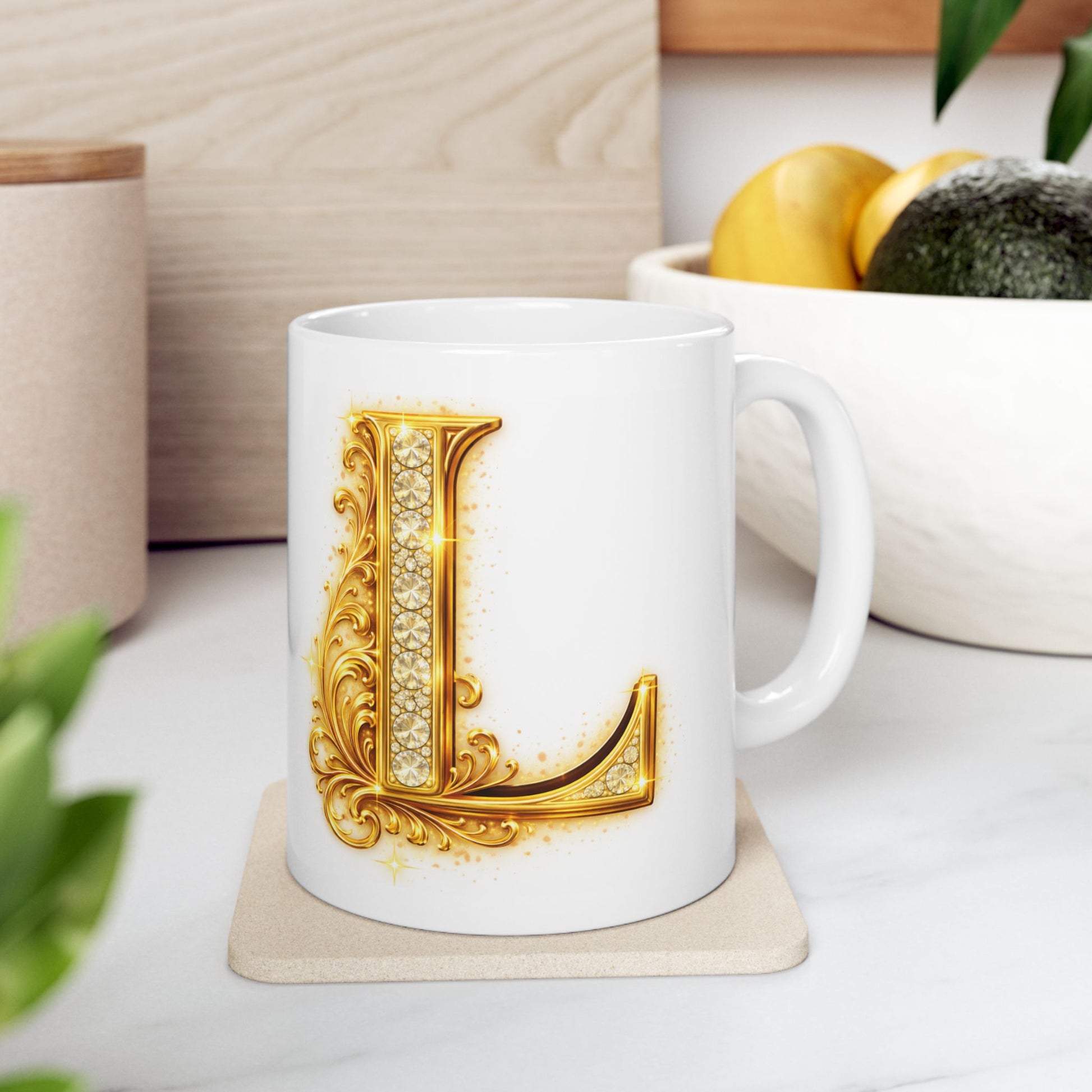 White mug with a gold letter 'L' design on a light surface with plants and a bowl in the background.