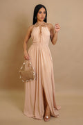 Woman wearing a beige halter neck dress holding a matching handbag against a beige background