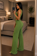 A woman takes a mirror selfie in a bedroom while wearing a bright green two-piece set consisting of a sleeveless crop top and matching high-waisted flared pants.