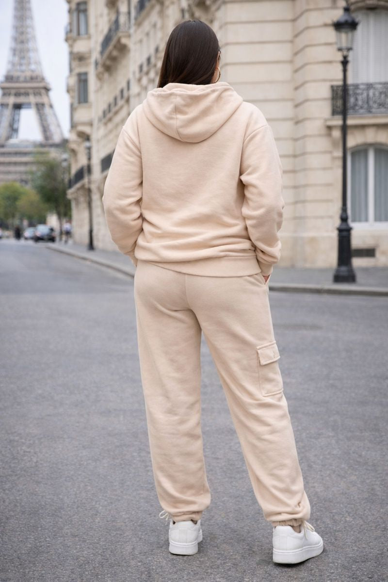 Person wearing a beige tracksuit walking on a street with the Eiffel Tower in the background