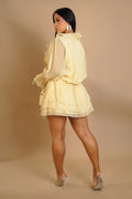 Woman wearing a light yellow layered dress against a beige background
