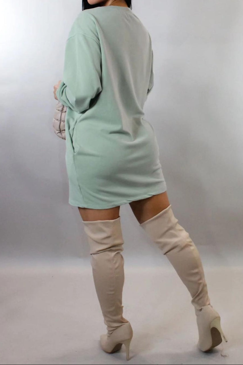 Woman wearing a light green dress and beige knee-high boots against a plain background
