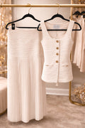 White pleated skirt and buttoned top on hangers against a neutral background