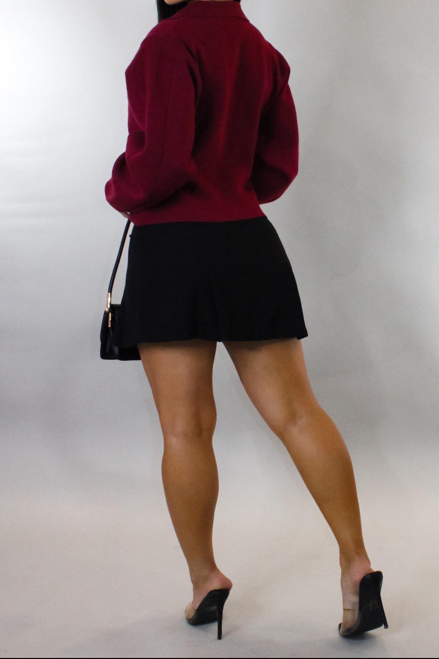 Woman wearing a red sweater and black skirt against a plain background