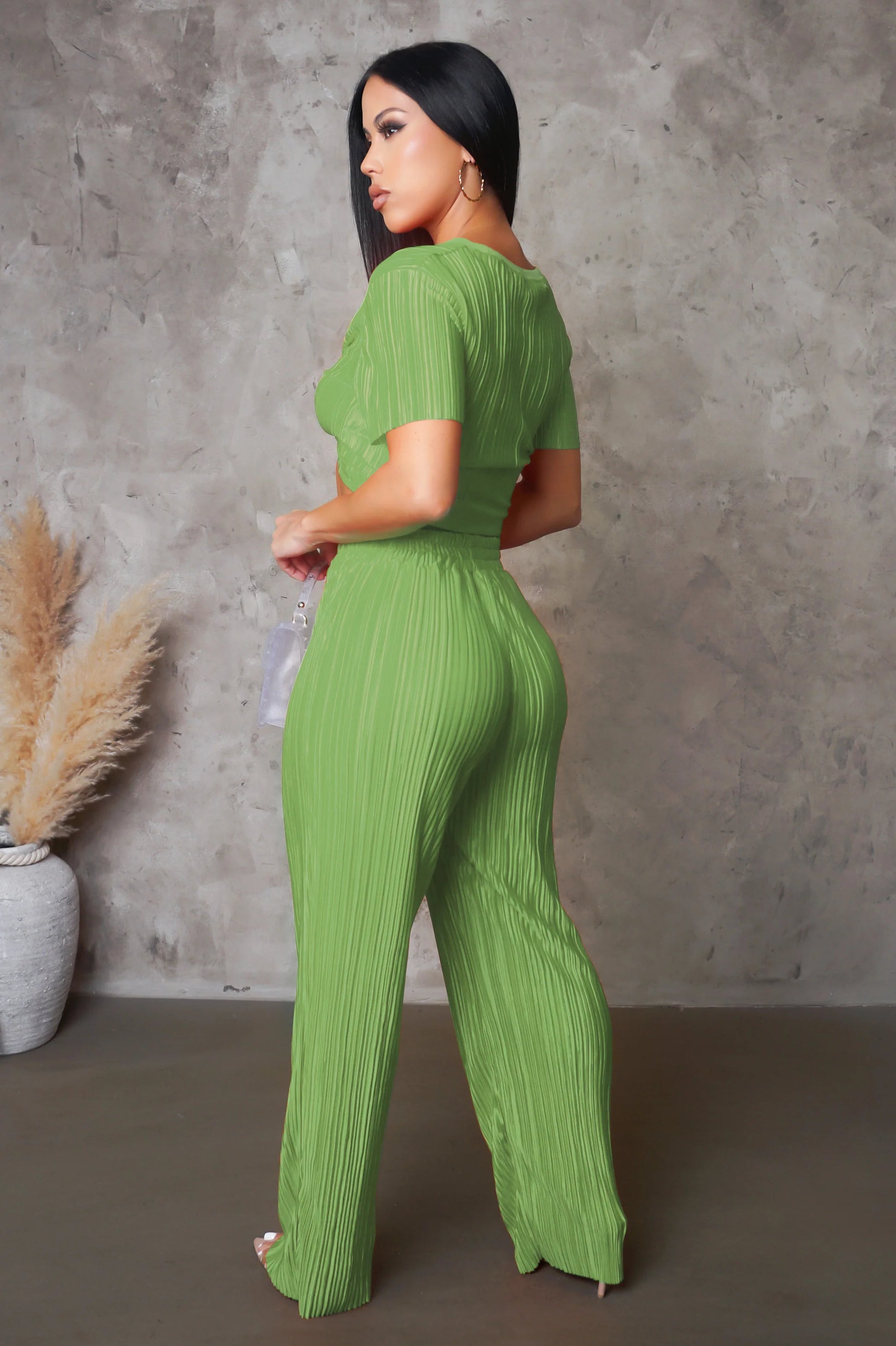 Woman wearing a green ribbed jumpsuit against a gray concrete wall.