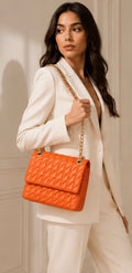 Woman holding an orange quilted handbag against a neutral background