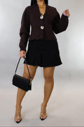 Woman wearing a brown blazer and skirt set with a black handbag on a white background