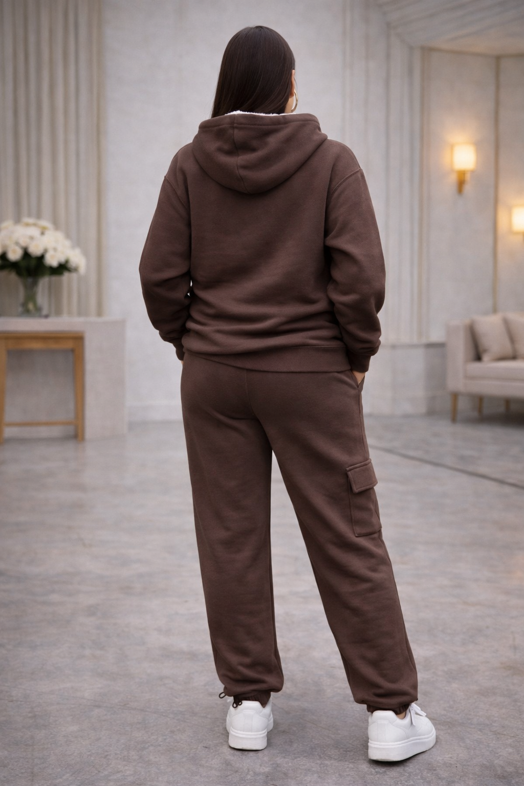 Woman wearing a brown tracksuit with 'alo' branding in a modern indoor setting.