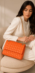 Woman holding an orange quilted handbag in a neutral setting