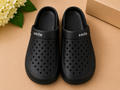 Black clogs with 'smile' text on a beige surface with flowers and a box in the background