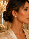 Close-up of a woman wearing a large cubic zirconia earring with a blurred chandelier in the background.
