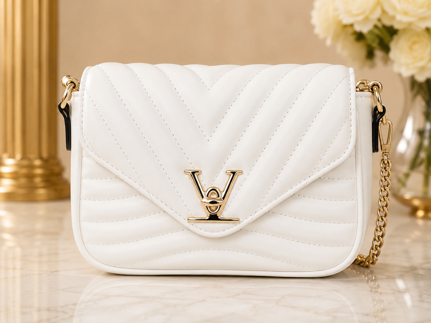 A white quilted leather shoulder bag with a gold-tone LV logo clasp and chain strap, displayed on a marble surface with a gold column and flowers in the background.