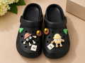 Black clogs with decorative charms on a beige surface