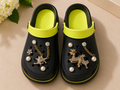Black clogs with lime green accents and decorative brooches on a beige surface.