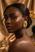 A close-up portrait of a woman with dark hair pulled back, wearing a large textured gold hoop earring. The background consists of draped gold satin fabric.