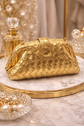 Gold woven handbag on a marble surface with decorative items
