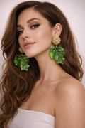 Woman wearing green leaf-shaped earrings with a plain background