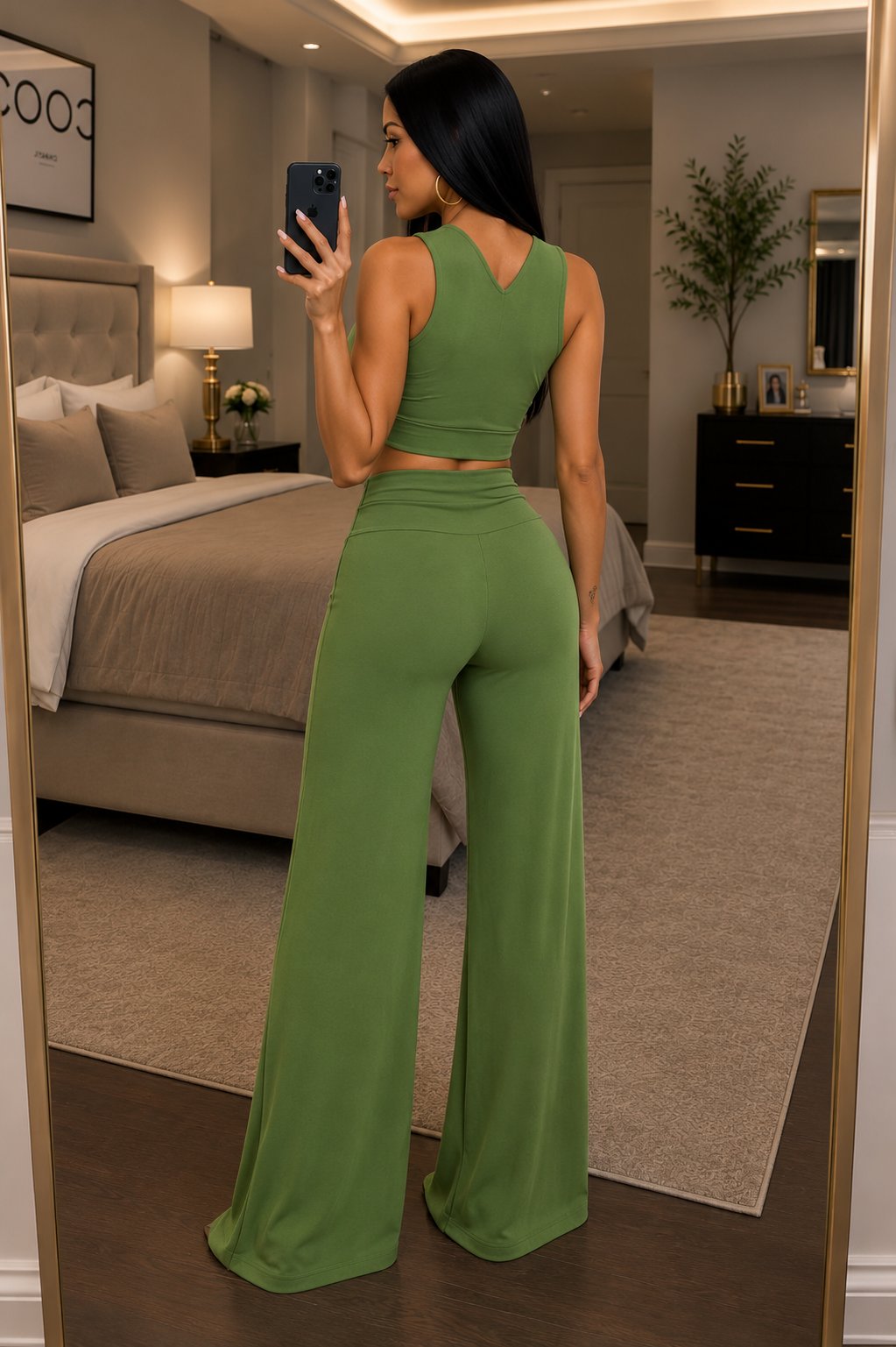 A woman takes a mirror selfie in a bedroom wearing a matching olive green two-piece set consisting of a halter crop top and high-waisted wide-leg pants, accessorized with a gold circular necklace.