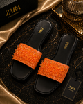 Black slides with orange gemstones on a Zara branded surface