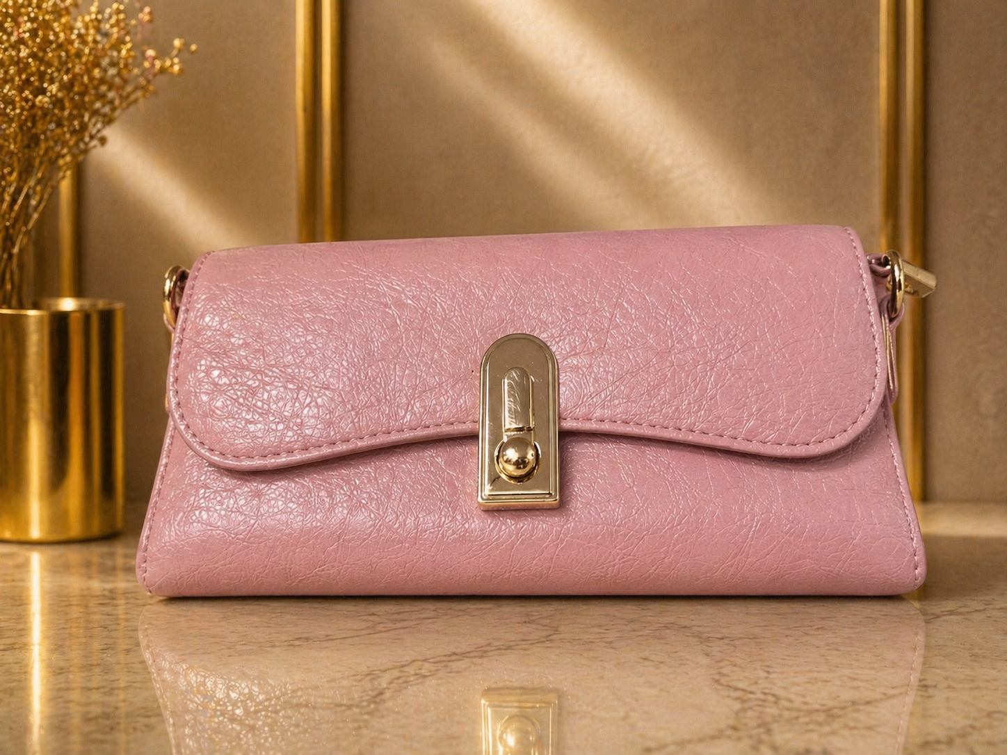 Pink handbag with gold clasp on a reflective surface with a gold frame background