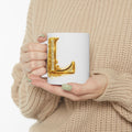 Person holding a mug with a decorative letter 'L' design, wearing a beige sweater.