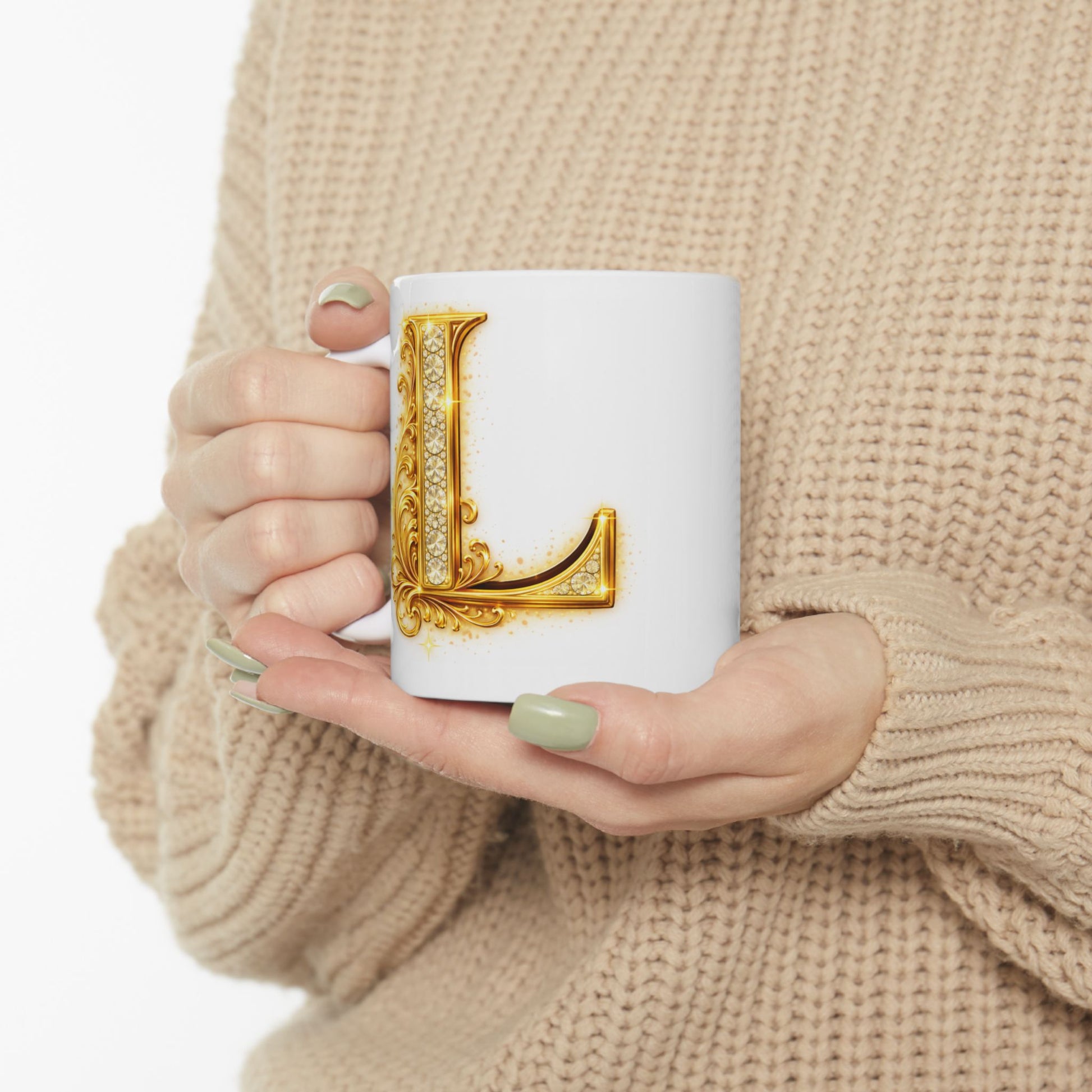 Person holding a mug with a decorative letter 'L' design, wearing a beige sweater.