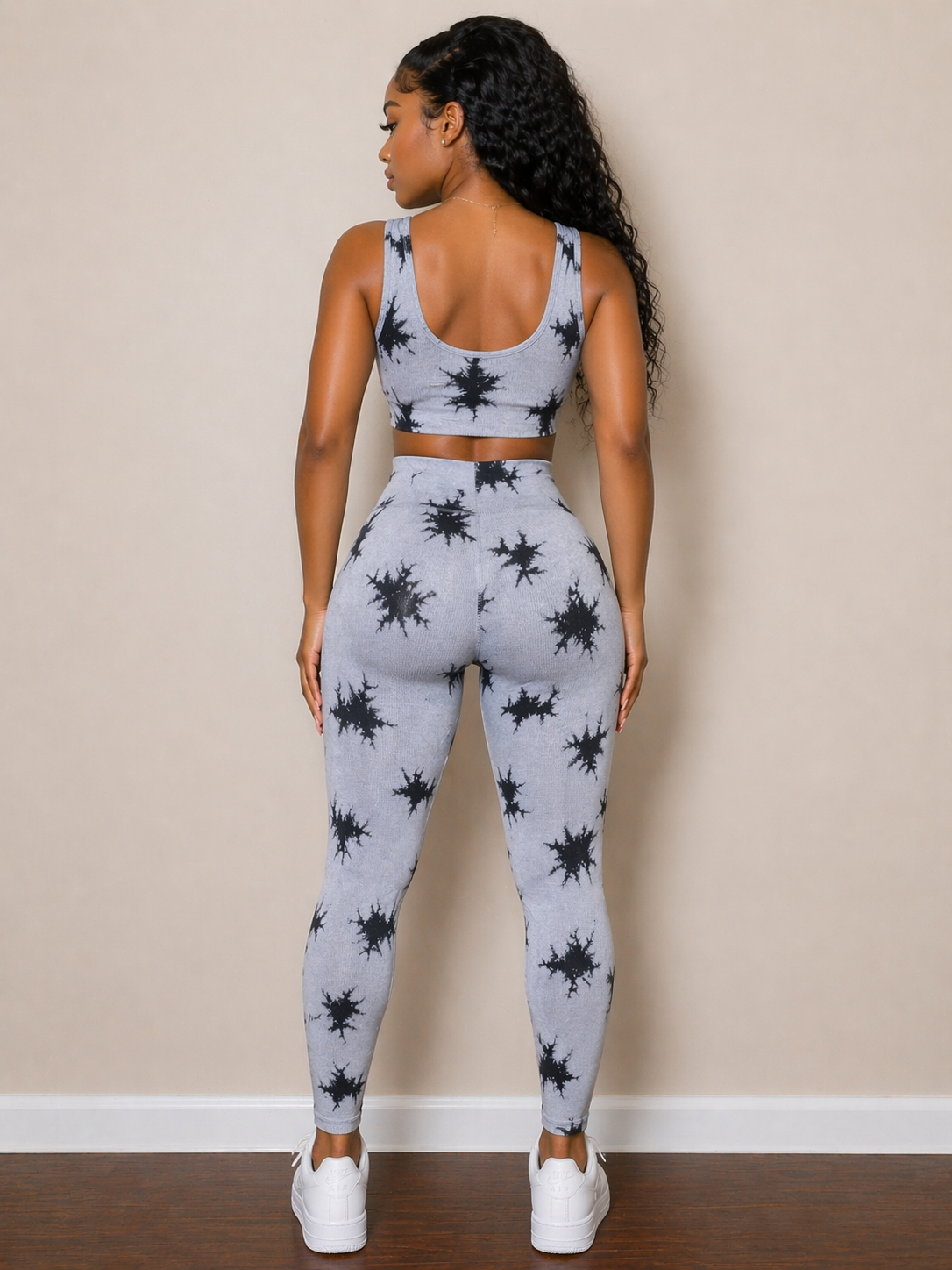 Woman wearing a gray and black patterned athletic outfit against a beige wall.