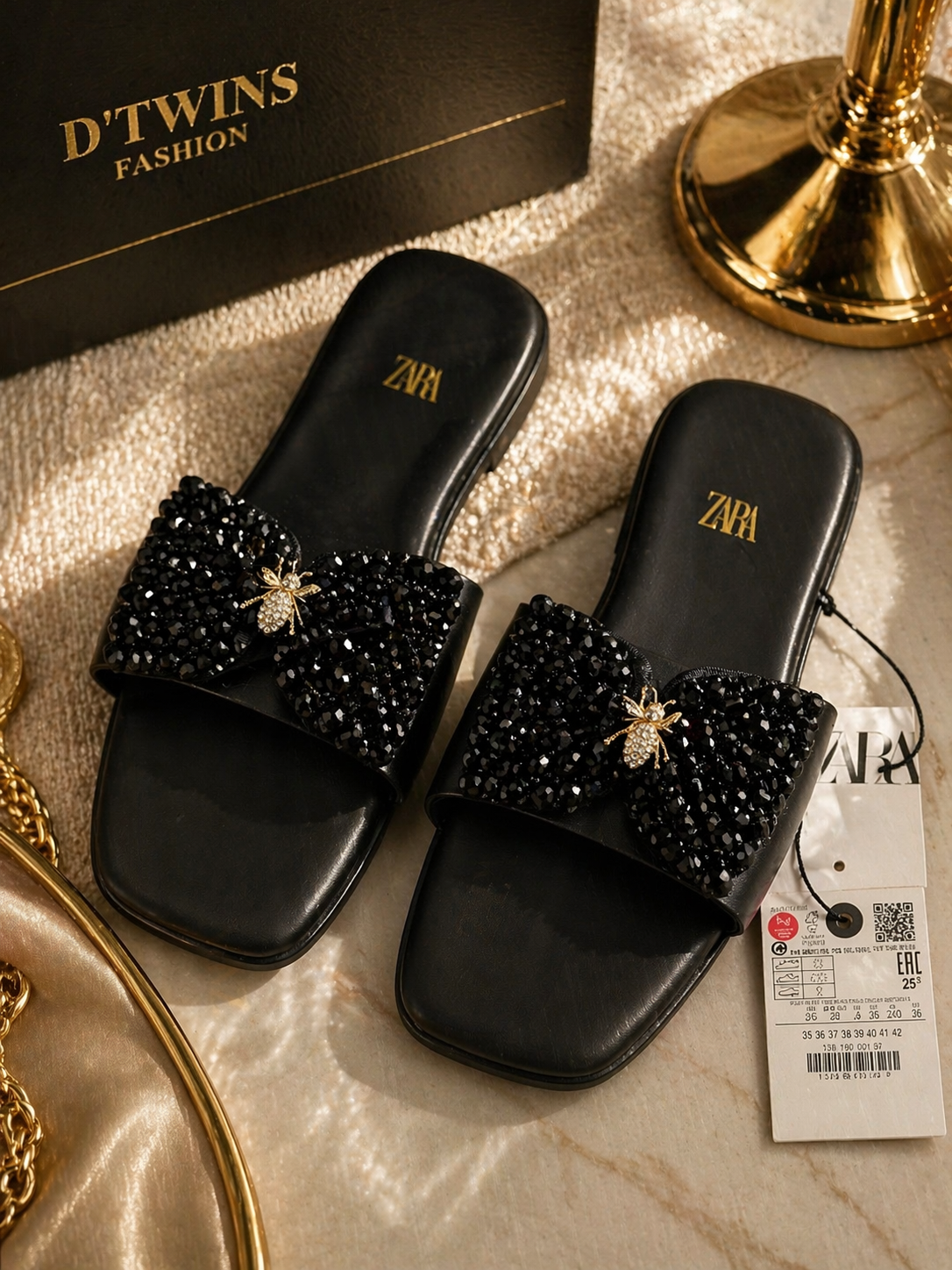 Black embellished slides with 'Zara' branding on a gold surface next to a Zara tag.