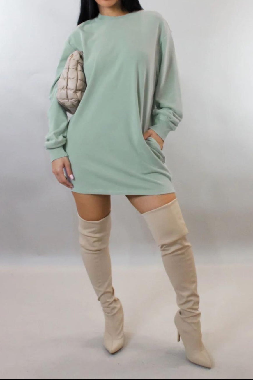 Woman wearing a light green oversized sweater dress with beige knee-high boots on a plain background