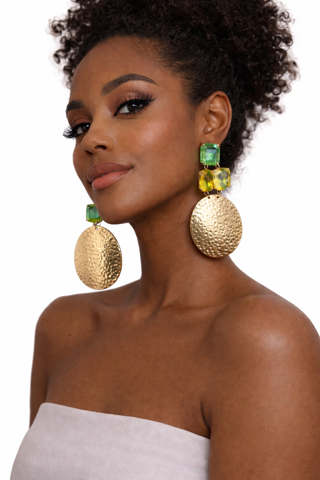 Woman wearing large gold earrings with green gemstones on a white background