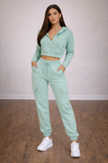 Woman wearing a mint green tracksuit with white sneakers on a wooden floor.