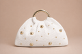 White handbag with gold studs on a beige background