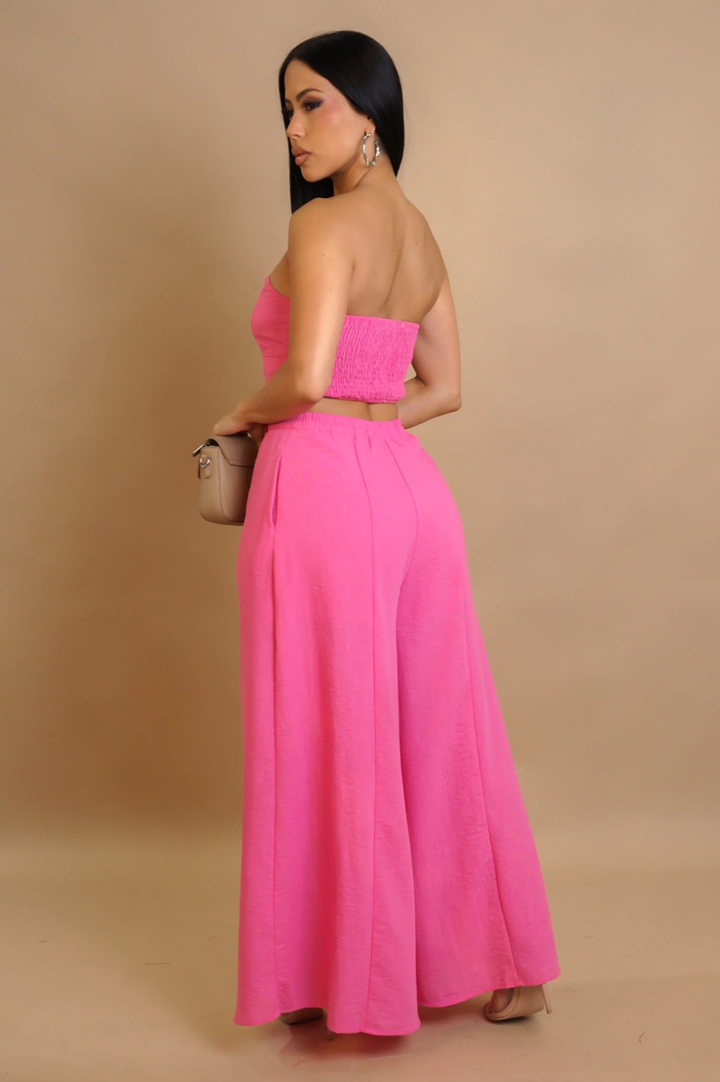 Woman wearing a bright pink strapless top and wide-leg pants against a beige background